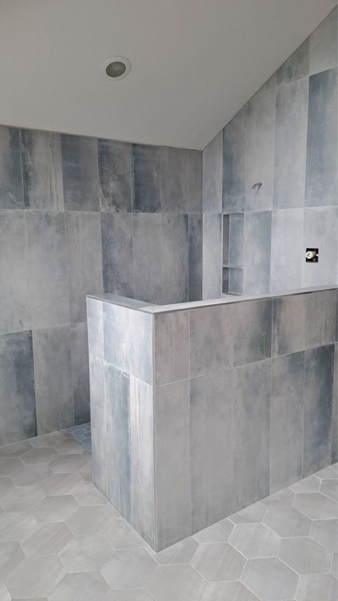 Shower with large gray tile and a half wall