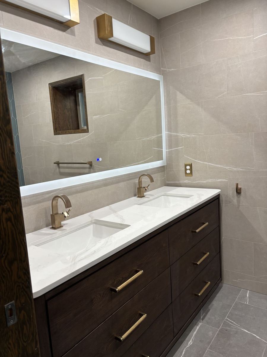 Remodeled bathroom with a dark wood vanity and a large lit mirror