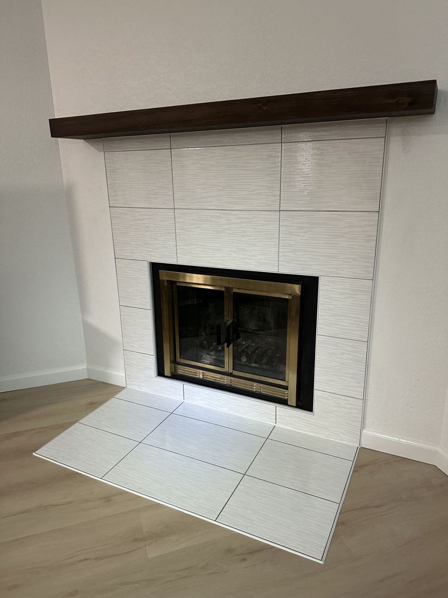 White tile fireplace surround with a wood mantel